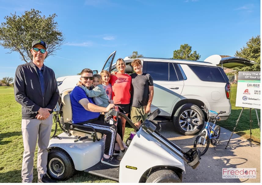 Adam with his family at the 2024 Veterans Day Golf Challenge in a Solo Rider in front of his donated Tahoe from Matt and Dr. Jean Tuggey.